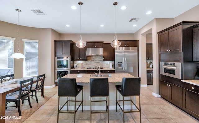 kitchen with appliances with stainless steel finishes, a kitchen island with sink, sink, and decorative light fixtures