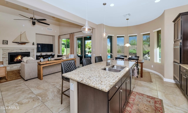 kitchen featuring pendant lighting, sink, a breakfast bar, dark brown cabinets, and a center island with sink