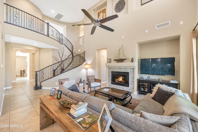 tiled living room with ceiling fan, a stone fireplace, and a towering ceiling