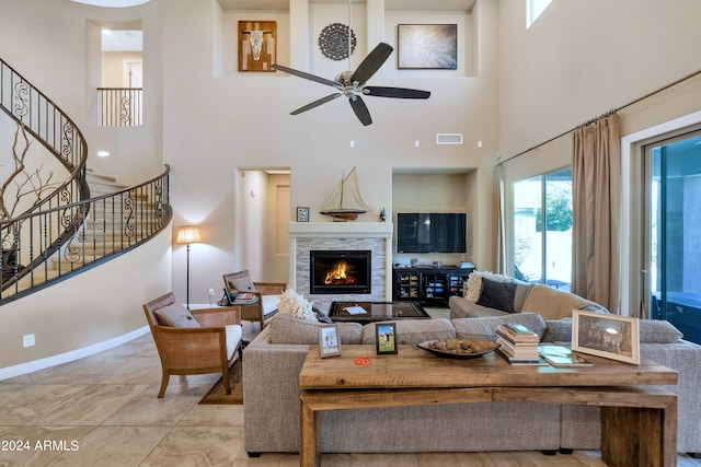 living room with a stone fireplace, a towering ceiling, and ceiling fan