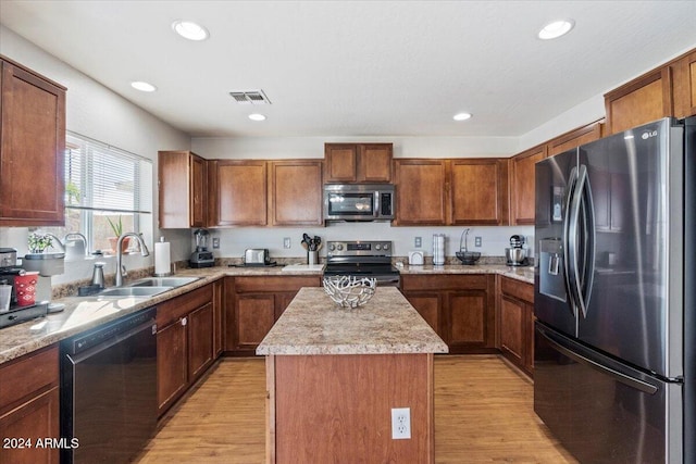 kitchen with appliances with stainless steel finishes, light hardwood / wood-style flooring, a center island, and sink