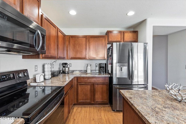 kitchen with appliances with stainless steel finishes, light stone countertops, and light hardwood / wood-style floors