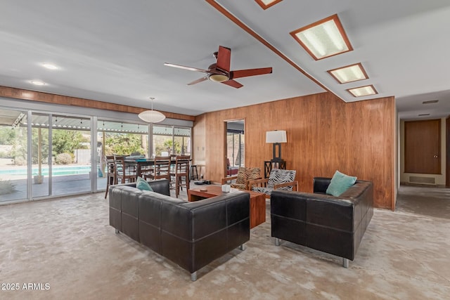 living room with a ceiling fan, concrete floors, visible vents, and wood walls