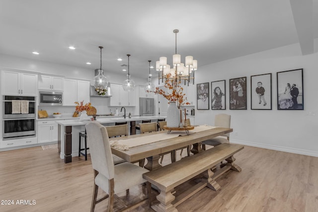 dining space with light wood-type flooring, sink, and a chandelier