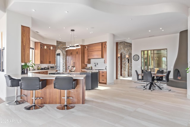 kitchen with arched walkways, brown cabinetry, a peninsula, light countertops, and a kitchen bar