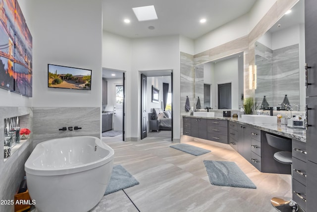 ensuite bathroom with a skylight, a sink, a towering ceiling, a soaking tub, and double vanity