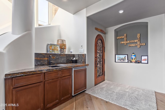 bar with indoor wet bar, a sink, decorative backsplash, and wood finished floors