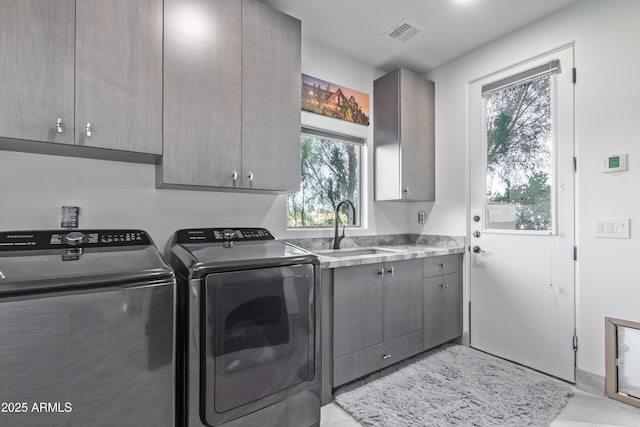 clothes washing area with cabinet space, a sink, visible vents, and washing machine and clothes dryer