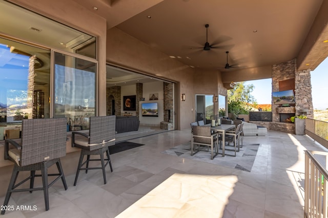 view of patio featuring outdoor dining space, an outdoor stone fireplace, and ceiling fan