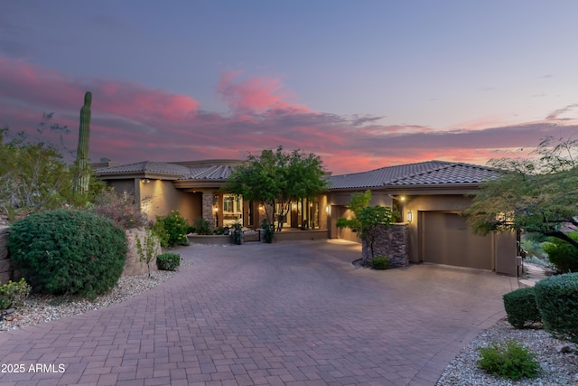 view of front facade featuring decorative driveway, an attached garage, a tile roof, and stucco siding