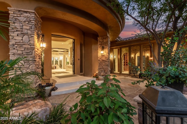 exterior entry at dusk featuring stone siding, a patio, and stucco siding