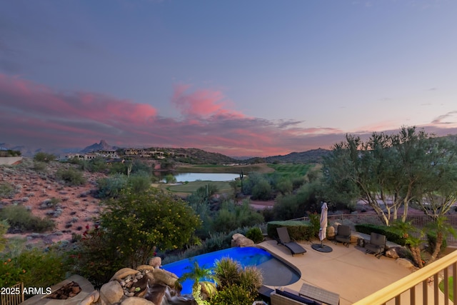 pool at dusk with an infinity pool, a patio area, and a water view