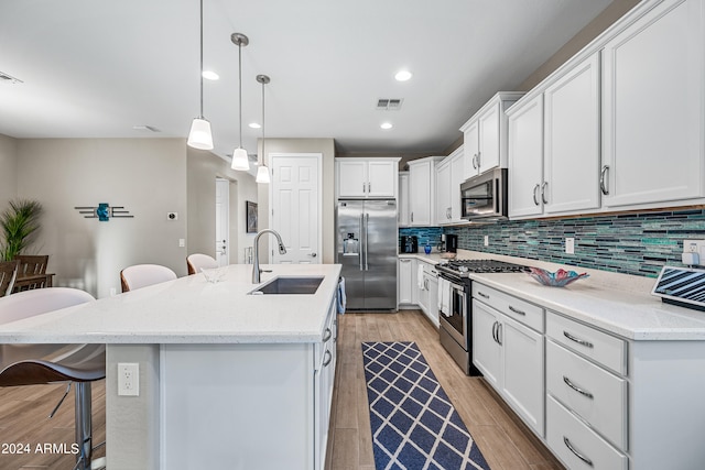 kitchen with appliances with stainless steel finishes, sink, white cabinets, hanging light fixtures, and a center island with sink