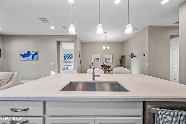 kitchen with light stone counters, sink, pendant lighting, and white cabinetry