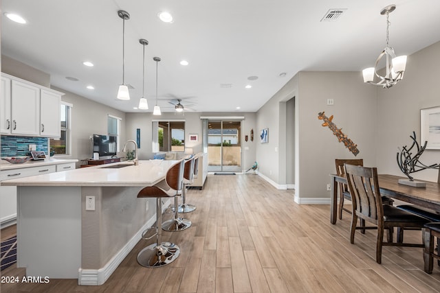 kitchen featuring white cabinetry, sink, decorative light fixtures, and an island with sink