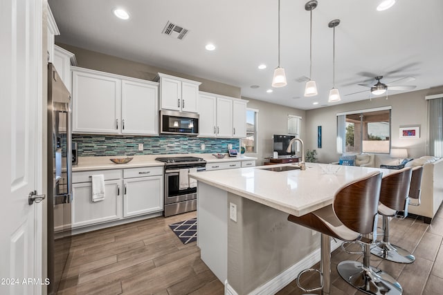 kitchen with a kitchen island with sink, sink, white cabinets, and appliances with stainless steel finishes