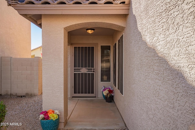 entrance to property featuring fence, a tiled roof, and stucco siding