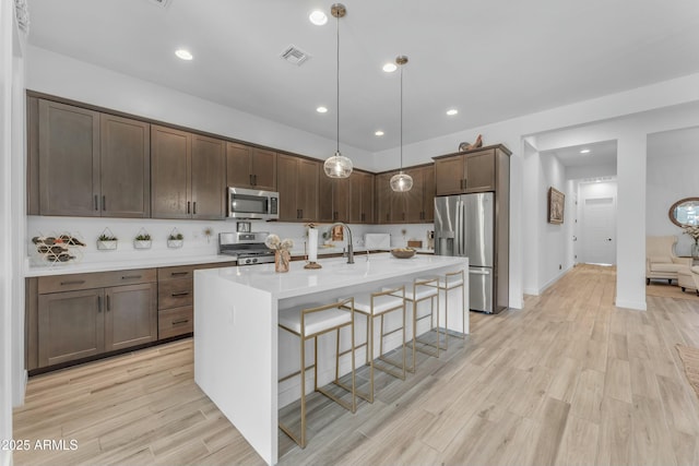 kitchen with decorative light fixtures, a kitchen breakfast bar, light hardwood / wood-style flooring, and stainless steel appliances