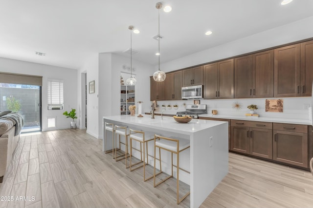 kitchen featuring appliances with stainless steel finishes, dark brown cabinets, pendant lighting, an island with sink, and a breakfast bar area