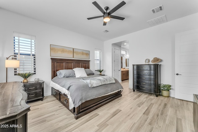 bedroom featuring ceiling fan, light hardwood / wood-style flooring, multiple windows, and ensuite bath