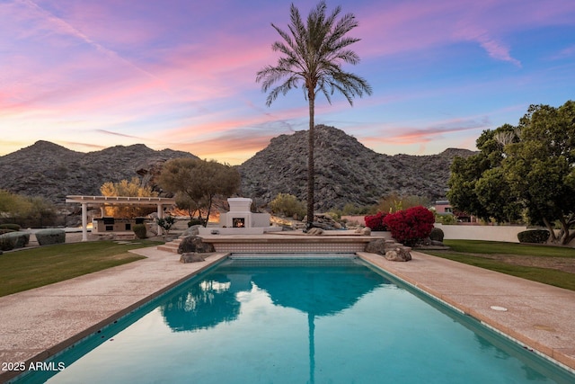 11809 S Montezuma Ct, Phoenix, AZ 85044 - pool at dusk with a lit fireplace, a mountain view, a patio area, a lawn, and an outdoor pool