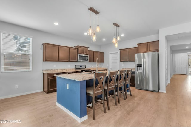 696 W Glen Canyon Dr, San Tan Valley, AZ 85140 - kitchen featuring a breakfast bar, an island with sink, appliances with stainless steel finishes, light wood finished floors, and hanging light fixtures