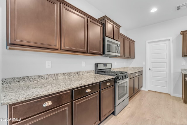 696 W Glen Canyon Dr, San Tan Valley, AZ 85140 - kitchen with visible vents, light stone counters, stainless steel appliances, light wood-style floors, and dark brown cabinets