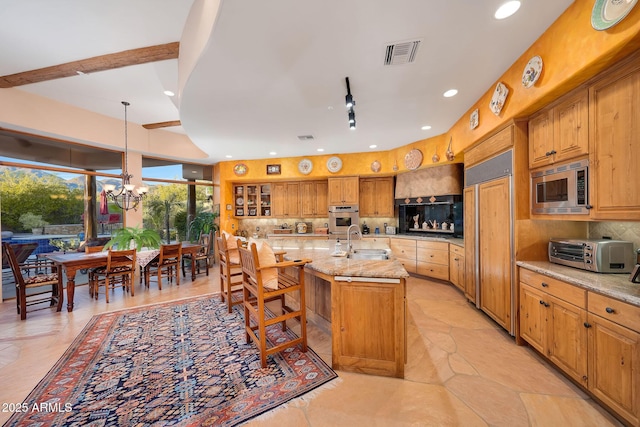 kitchen featuring light stone countertops, sink, built in appliances, a chandelier, and a center island with sink