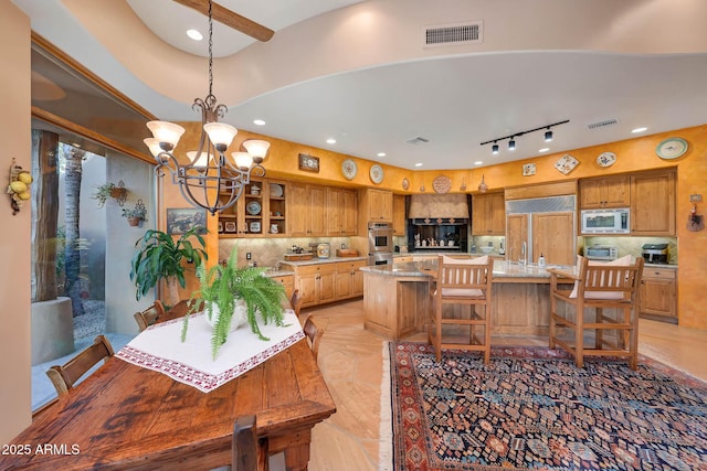 interior space with built in appliances, decorative light fixtures, a kitchen island, light stone counters, and a chandelier