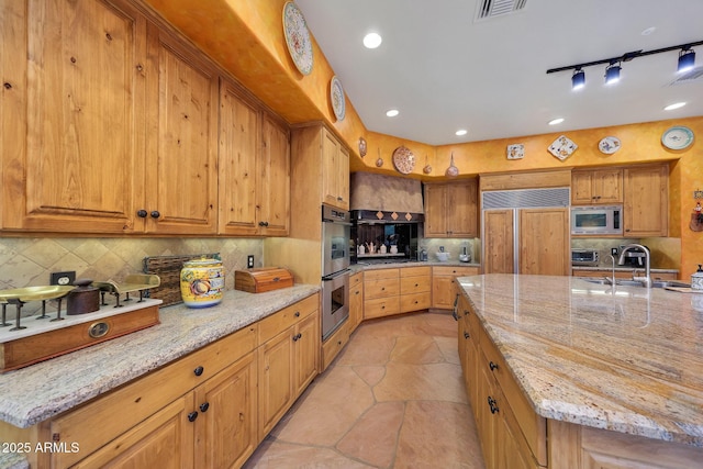 kitchen with built in appliances, a spacious island, light stone countertops, and sink