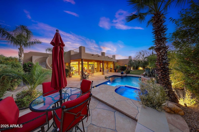 pool at dusk featuring an in ground hot tub and a patio area