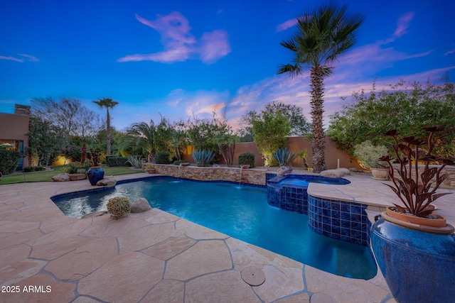 pool at dusk featuring pool water feature, a patio area, and an in ground hot tub