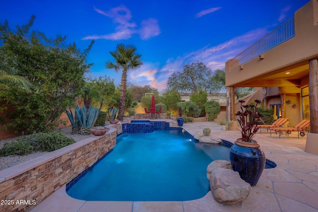 pool at dusk featuring an in ground hot tub, pool water feature, and a patio area