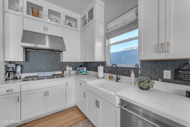 kitchen featuring stainless steel appliances, light stone countertops, decorative backsplash, light hardwood / wood-style floors, and white cabinets