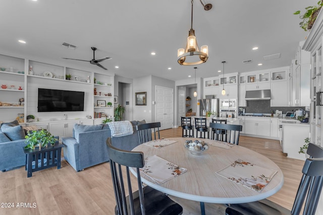 dining space with ceiling fan with notable chandelier and light hardwood / wood-style flooring