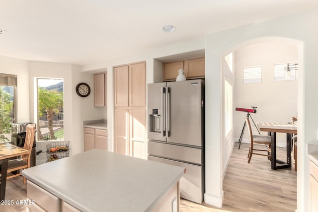 kitchen with light countertops, light wood finished floors, high end refrigerator, a center island, and arched walkways