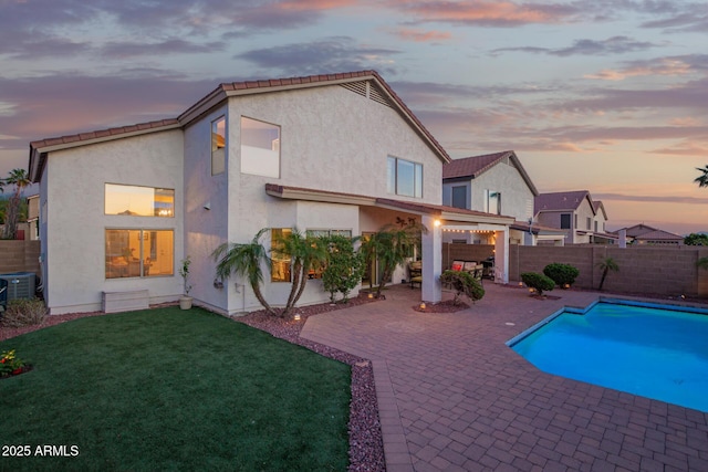 back of property at dusk featuring a patio, a fenced backyard, a lawn, and stucco siding