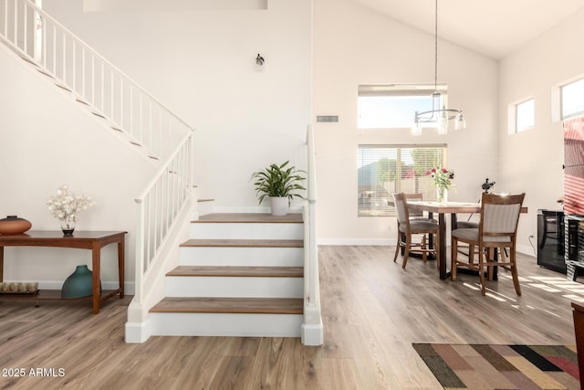 stairs with wood finished floors, high vaulted ceiling, a chandelier, and visible vents