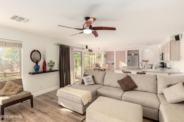living area with baseboards, visible vents, light wood-style flooring, and a ceiling fan