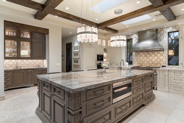 kitchen featuring pendant lighting, appliances with stainless steel finishes, premium range hood, a spacious island, and dark brown cabinetry