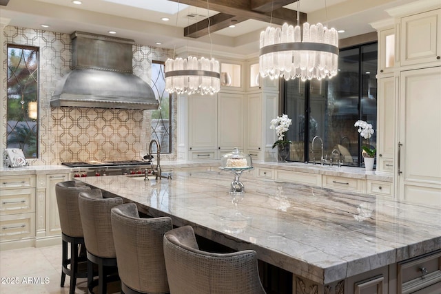 kitchen featuring a large island, sink, light stone counters, custom range hood, and a kitchen bar