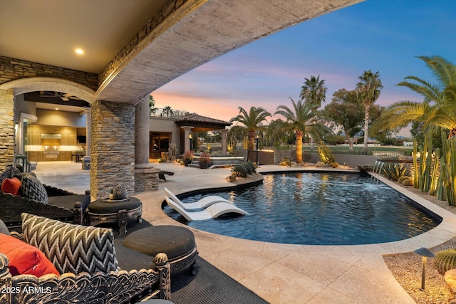 pool at dusk with pool water feature, an outdoor hangout area, and a patio area