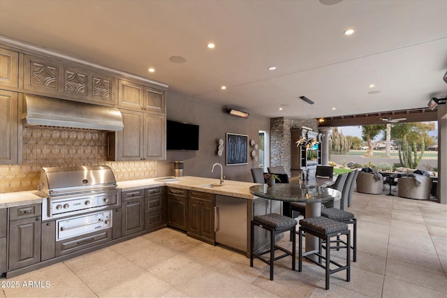 kitchen with sink, a breakfast bar area, refrigerator, premium range hood, and backsplash