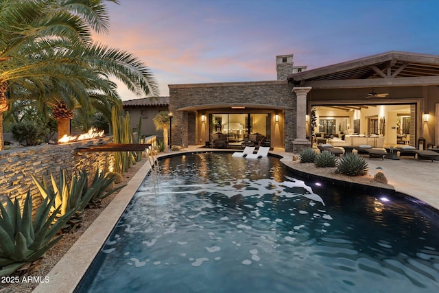 pool at dusk with a patio, outdoor lounge area, and ceiling fan