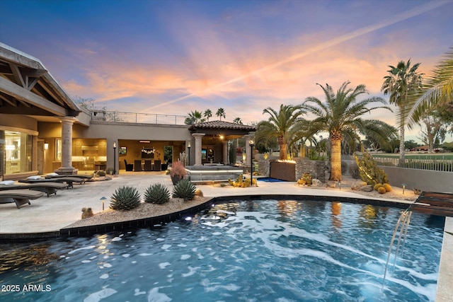 pool at dusk featuring a patio and pool water feature