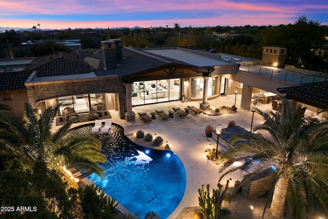 pool at dusk featuring a patio area and a multi sided fireplace