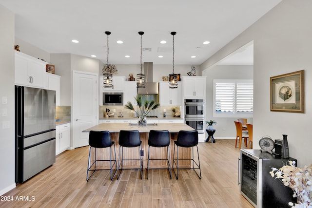 kitchen with hanging light fixtures, stainless steel appliances, backsplash, an island with sink, and white cabinets