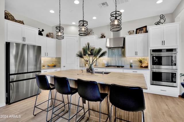 kitchen featuring wall chimney exhaust hood, white cabinetry, a kitchen island with sink, and appliances with stainless steel finishes