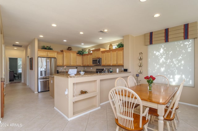 kitchen with light tile patterned floors, stainless steel appliances, kitchen peninsula, and light stone countertops