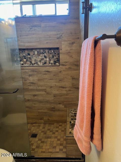 bathroom featuring a tile shower, toilet, and wooden walls